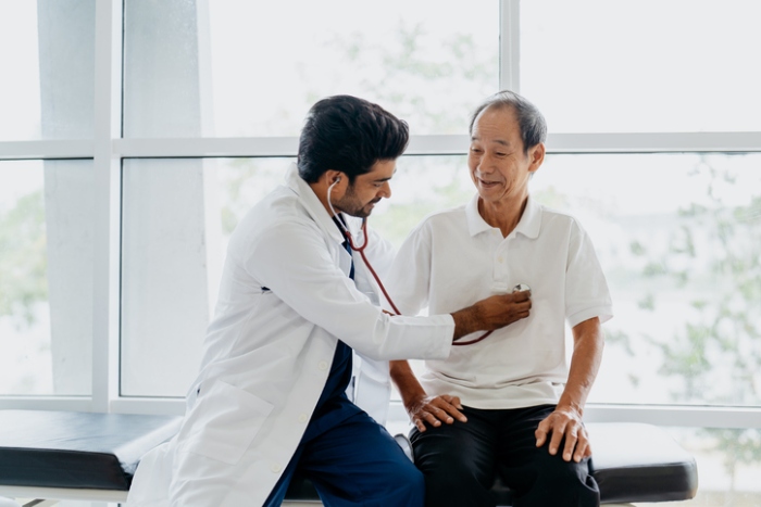 Doctor examining a senior male patient with a stethoscope in a clinic.