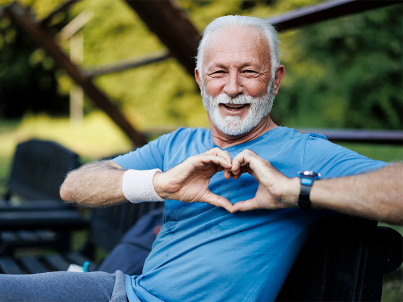 Person sitting outdoors making heart shape with hands